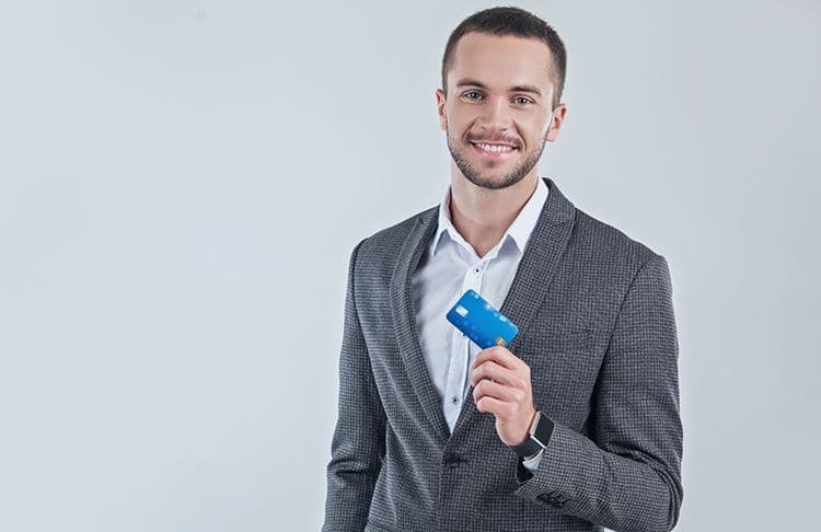 Mitarbeiter mit Firmenkarte – Abrechnung von Auslagen in der Lohnbuchhaltung Ein lächelnder Mann im Anzug hält eine blaue Karte in der Hand – symbolisch für die Nutzung von Firmenkarten und die Berücksichtigung solcher Auslagen in der Lohnbuchhaltung