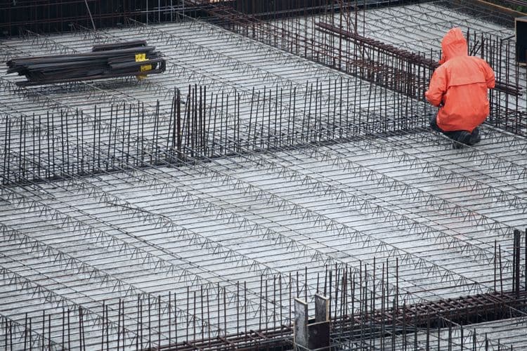 Bauarbeiter auf Baustelle – Relevanz für Lohnbuchhaltung im Baugewerbe Bauarbeiter in oranger Schutzkleidung kniet auf einer Bewehrungsmatte auf einer Baustelle – Symbol für Arbeitszeit- und Leistungsdokumentation in der Lohnbuchhaltung