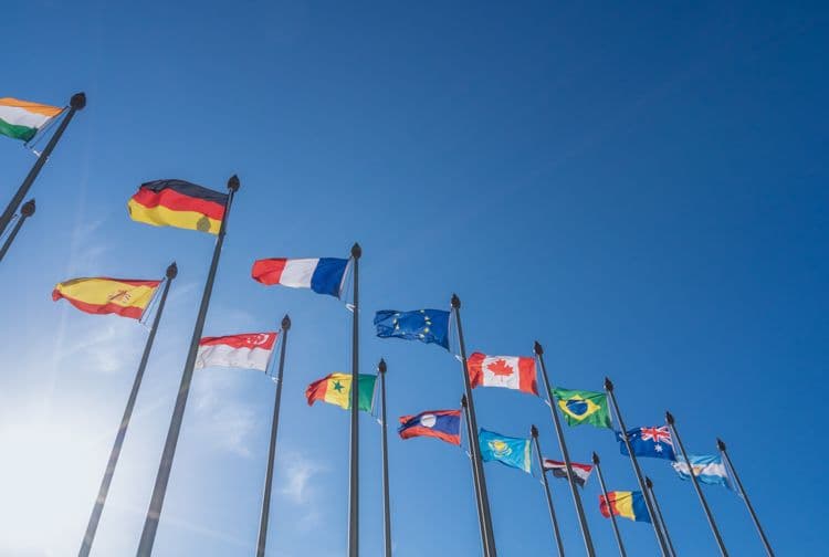 Internationale Flaggen vor blauem Himmel – Symbol für grenzüberschreitende Lohnabrechnung Verschiedene Nationalflaggen wehen im Wind vor klarem Himmel – geeignet für Themen der internationalen Lohnbuchhaltung und Mehrstaatenabrechnungen