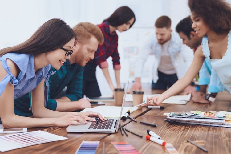 Junges Team bei gemeinsamer Arbeit an einem Projekttisch Mehrere junge Erwachsene arbeiten konzentriert gemeinsam an einem großen Tisch mit Laptop, Farbkarten, Markern und Notizbüchern