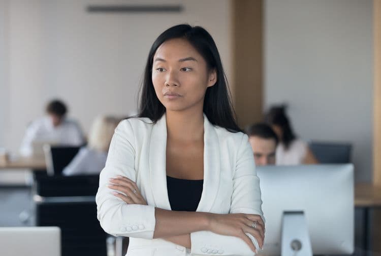 Nachdenkliche Führungskraft mit Verantwortung in der Lohnbuchhaltung Junge Frau in weißem Blazer steht mit verschränkten Armen im Büro und blickt konzentriert – symbolisiert Verantwortung in der Lohnbuchhaltung