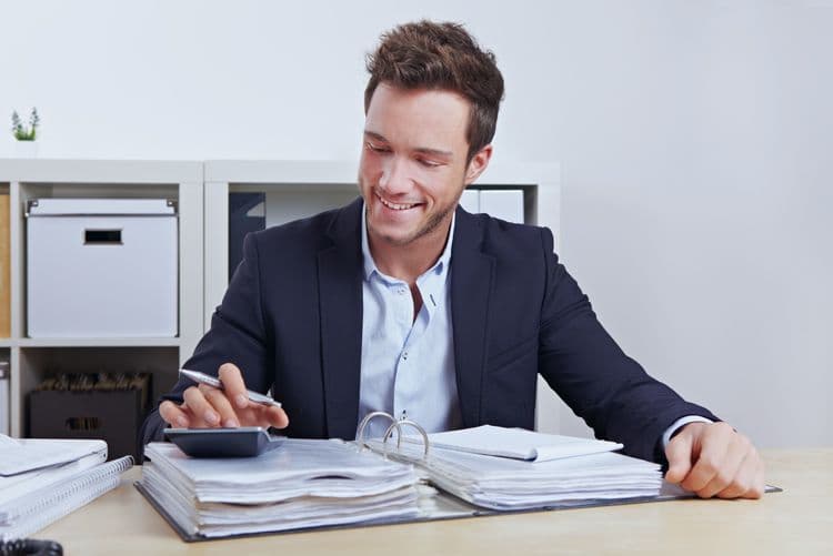 Effiziente Lohnbuchhaltung mit professioneller Abrechnungsstruktur Mann im Business-Outfit arbeitet mit Taschenrechner und Aktenordnern an der Lohnabrechnung