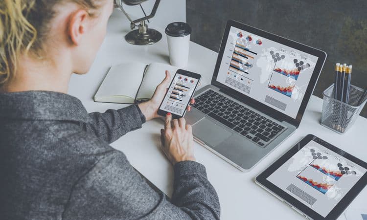 Digitale Auswertung von Lohndaten auf Laptop, Tablet und Smartphone Eine Lohnbuchhalterin betrachtet auf mehreren Geräten grafisch aufbereitete Lohndaten – auf Smartphone, Laptop und Tablet sind Diagramme und Karten sichtbar
